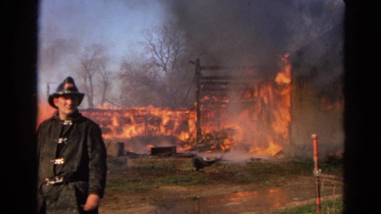 Firefighter walking toward the camera as a wooden barn burns behind him.