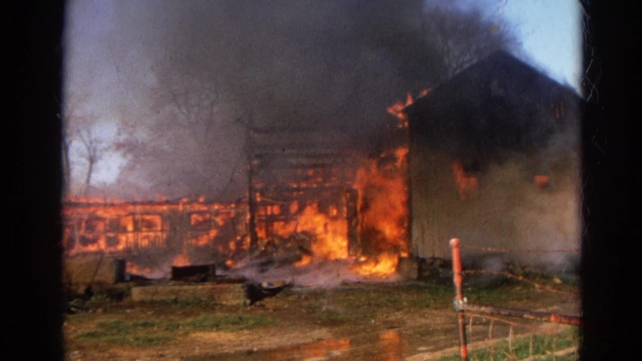 Flames and smoke engulf a farm building viewed through dark film gate edges.