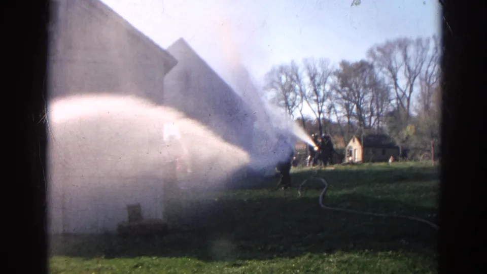1968 Wauconda, Illinois 8mm frame showing firefighters directing a hose stream at a smoke-filled farm building.