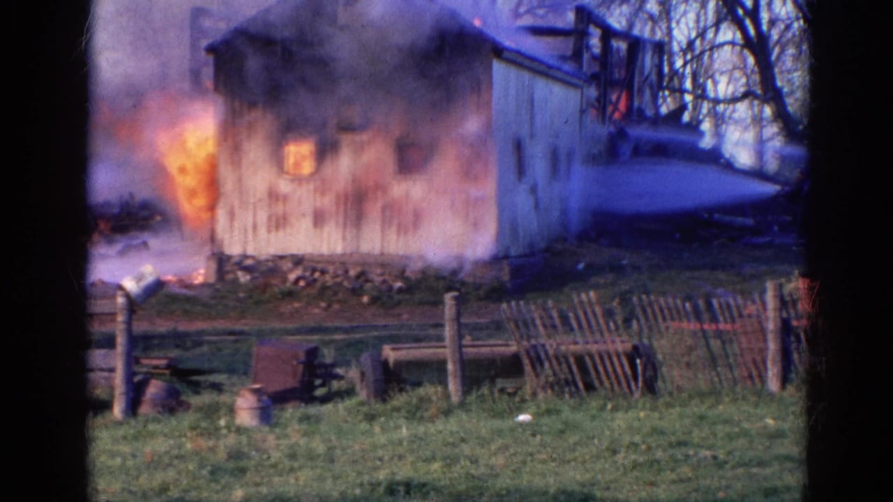 1968 Wauconda, Illinois 8mm frame showing a wooden barn engulfed in flames, with smoke, grass, fence posts, and farm equipment in front.