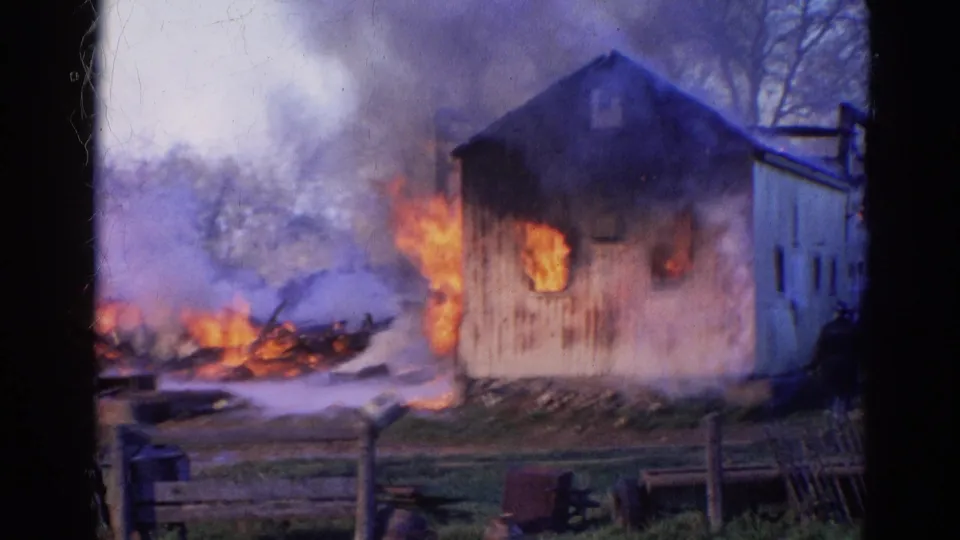 The barn burns in the right half of the frame while smoke and flames rise from debris in the yard, consistent with the Wauconda 1968 metadata.