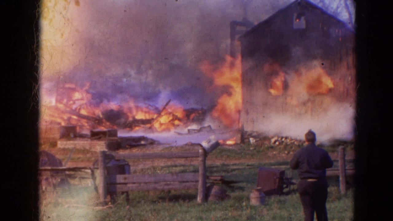 1968 Wauconda, Illinois 8mm frame showing a barn or outbuilding engulfed in flames with smoke, fencing, grass, and a distant observer.