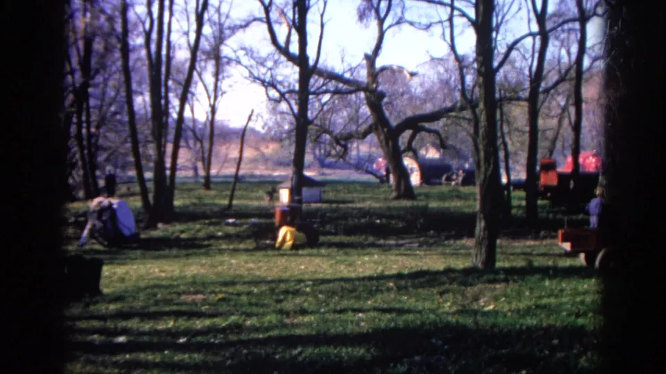 Wide 8mm view of the Wauconda fire area, with bare trees, grassy ground, smoke in the distance, and vehicles or equipment partly visible.