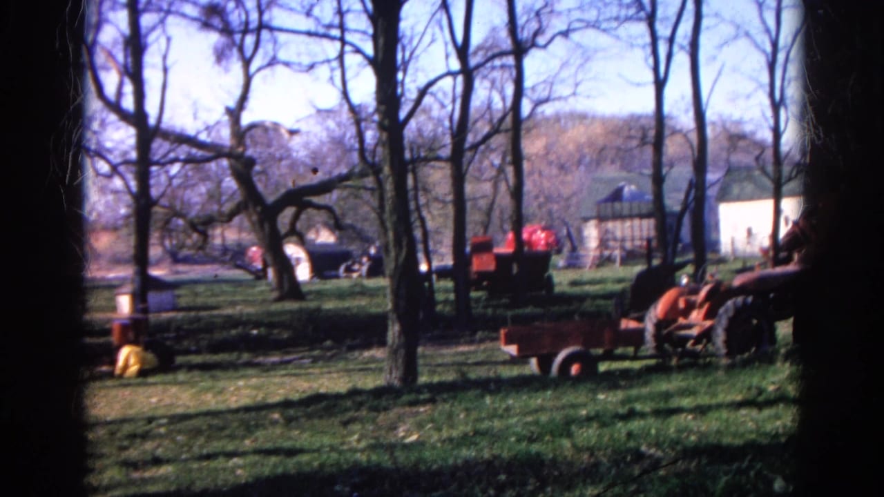 A rural Wauconda yard with leafless trees, red tractor equipment, wagons, and small outbuildings in faded 1968 8mm color.