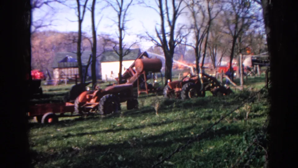 A red tractor and rust-colored farm machinery sit on a grassy Wauconda yard, with bare trees, outbuildings, and dark 8mm edge vignetting.