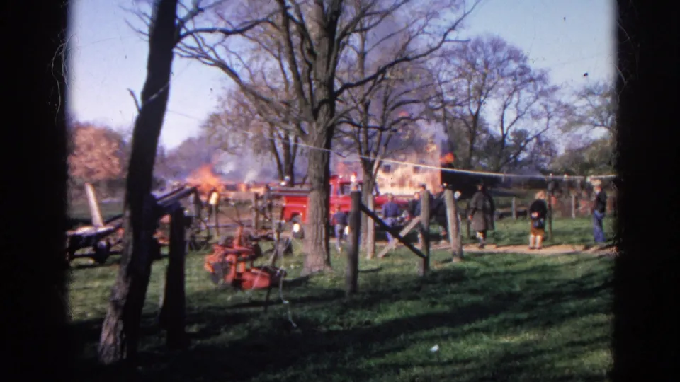 Wauconda farm scene with a red fire truck, onlookers, trees, fencing, and smoke or flames near outbuildings.