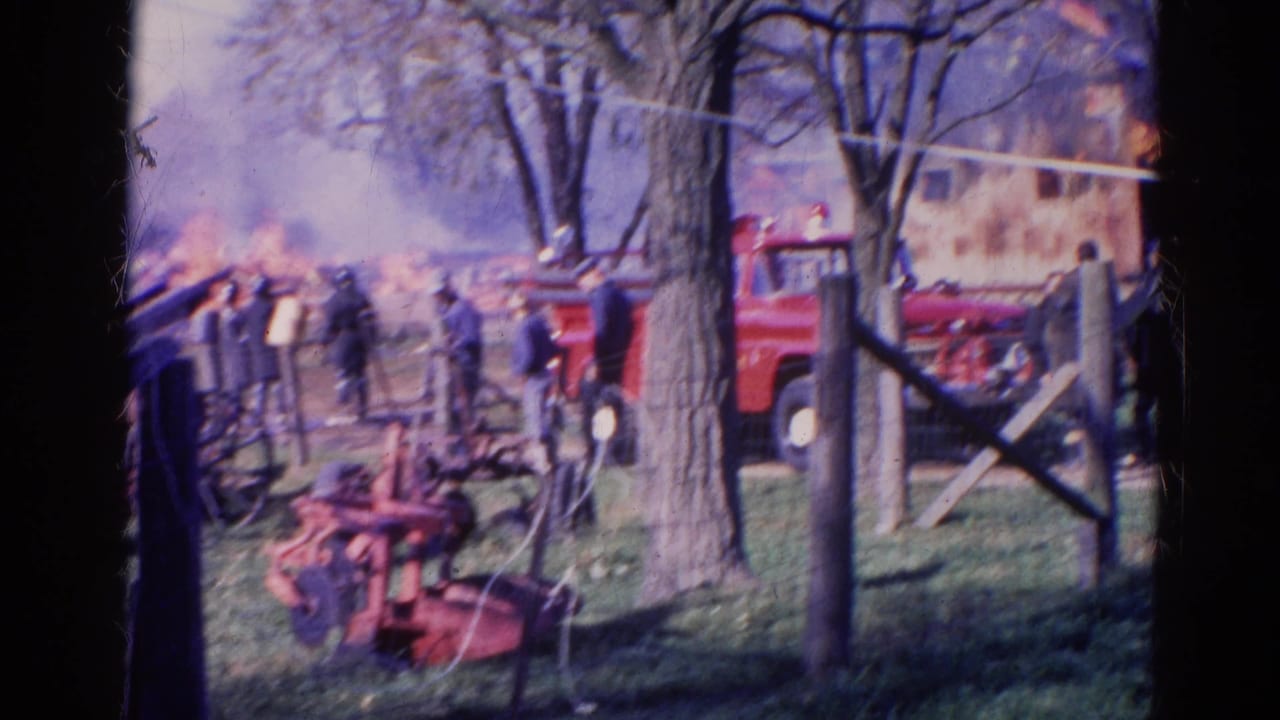 1968 Wauconda, Illinois home-movie frame showing a red fire truck, onlookers, smoke, flames, trees, and fencing near a rural fire.