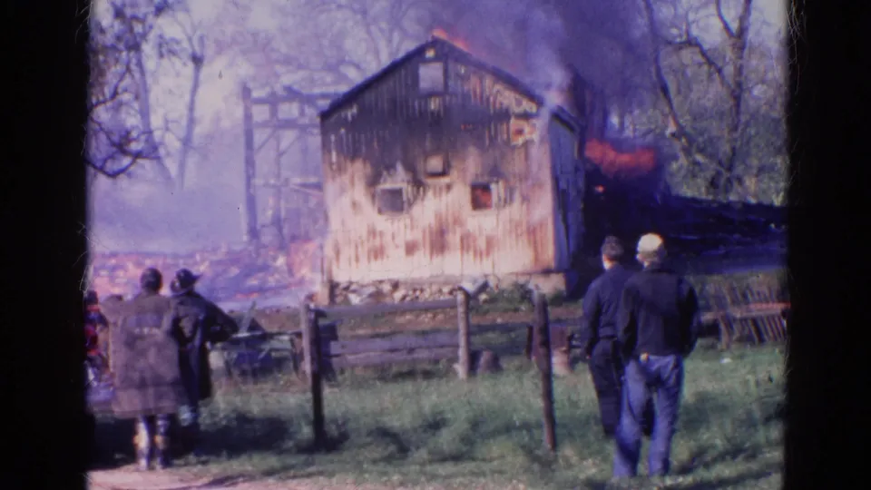Wauconda, Illinois fire scene with several people near a fence as flames and smoke surround a wooden building.