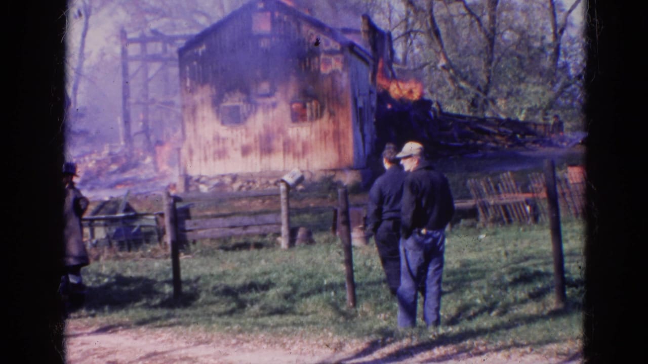 1968 Wauconda, Illinois 8mm frame showing people behind a fence watching flames on a wooden structure.
