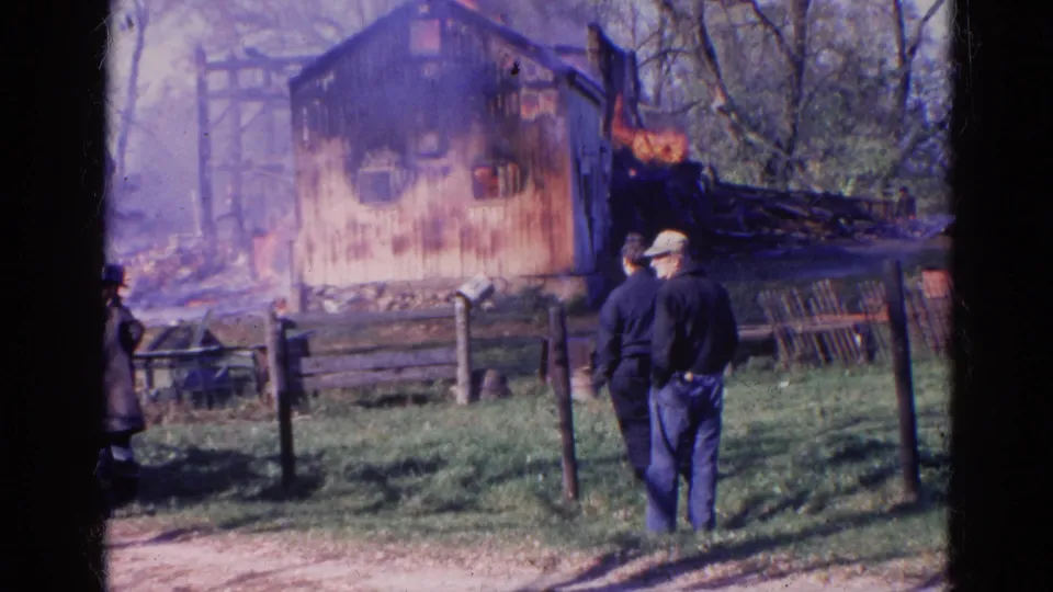 1968 Wauconda, Illinois 8mm frame showing people behind a fence watching flames on a wooden structure.