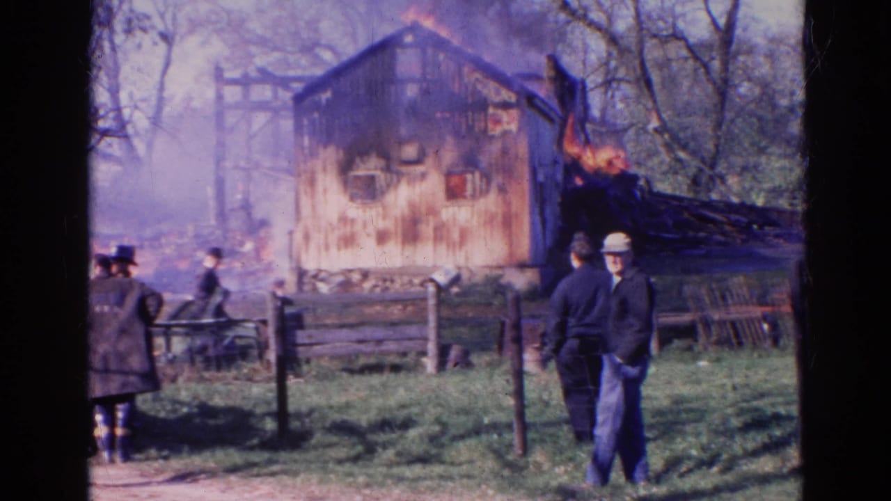 1968 Wauconda, Illinois home-movie frame of bystanders near a fence with a burning structure in the background.