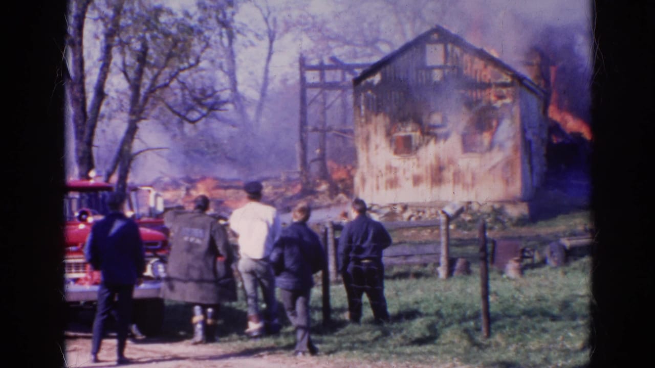 1968 Wauconda, Illinois frame showing onlookers near a red vehicle watching a wooden structure engulfed by fire.