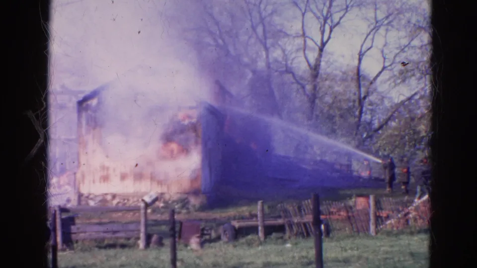 1968 Wauconda, Illinois frame showing the burning structure partly obscured by smoke as firefighters continue using hose lines.