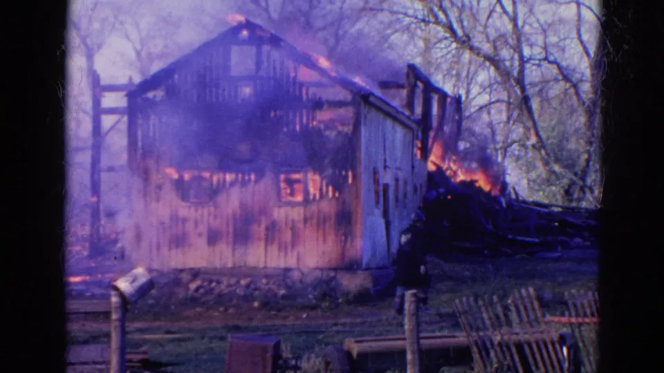 1968 Wauconda, Illinois frame with a barn burning intensely, smoke drifting across the structure, and yard posts in the foreground.