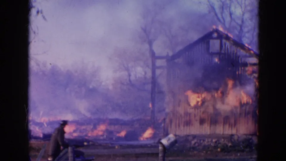 A person in dark clothing appears near the foreground as the burning wooden shed sends smoke across the Wauconda yard.