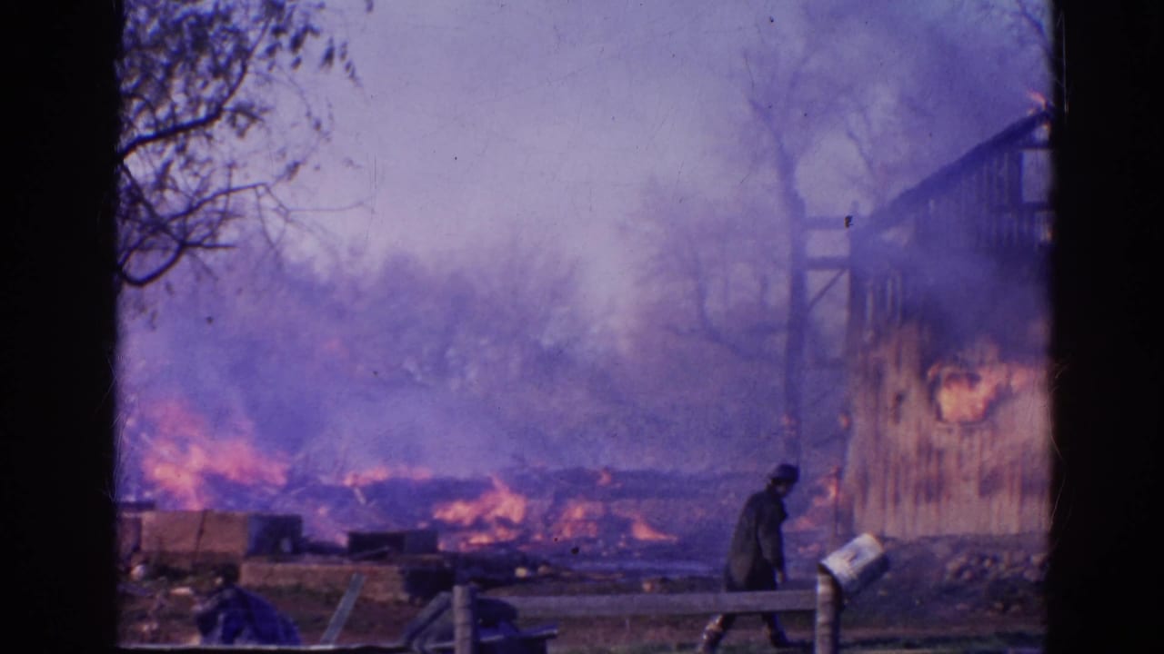 Heavy smoke drifts across the Wauconda fire scene as a dark-clothed figure stands near debris beside the burning structure.