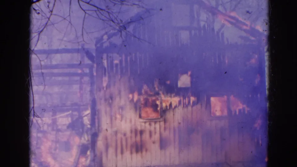 1968 Wauconda, Illinois 8mm frame showing flames inside a wooden building as smoke rises around bare trees.