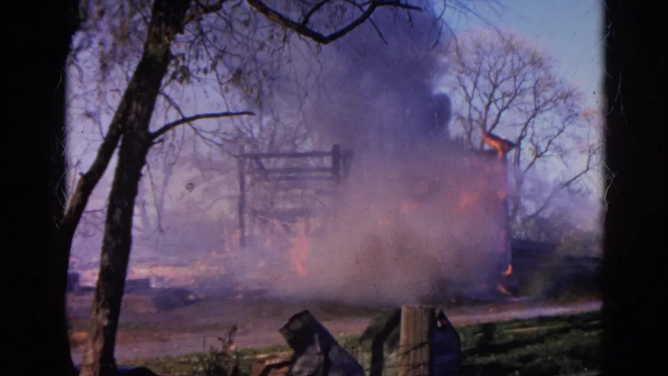 1968 Wauconda 8mm frame with dense smoke over a burning structure, orange flames, bare trees, and dark foreground framing.
