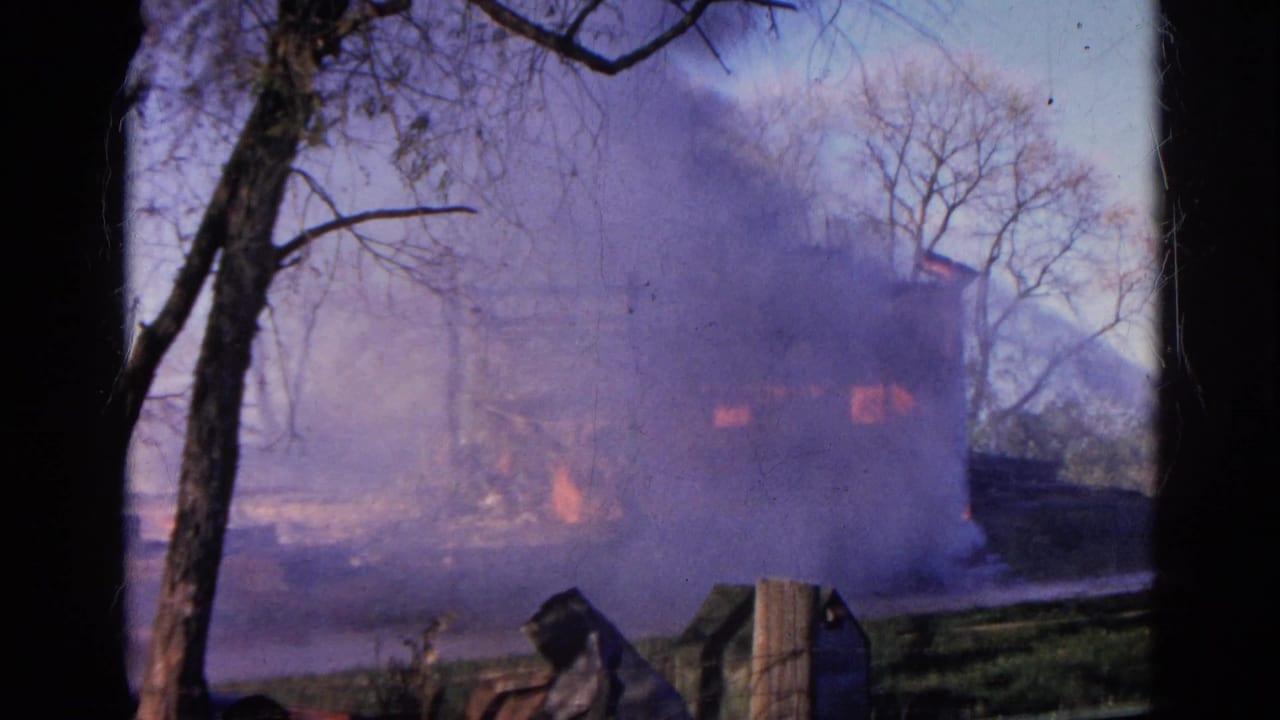 Burning two-story structure behind bare trees with heavy smoke and orange flames.