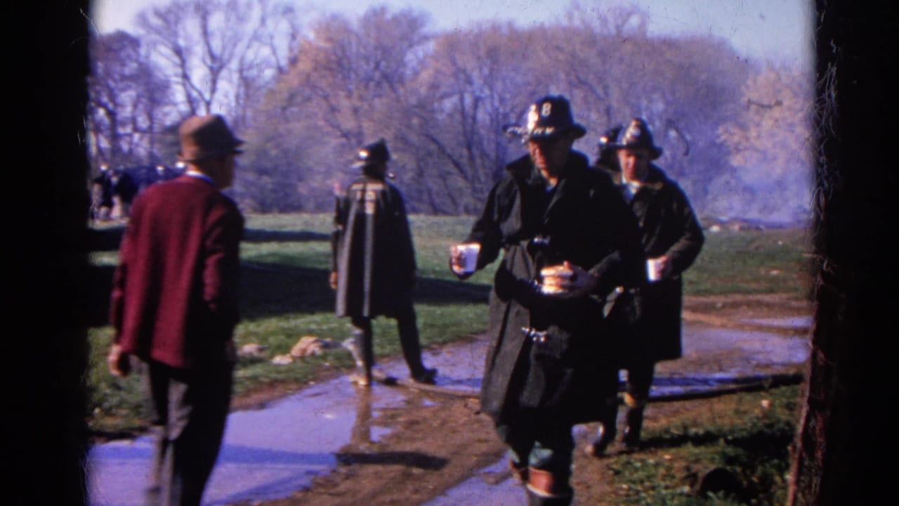 1968 Wauconda, Illinois 8mm frame showing firefighters in dark coats walking near a muddy path as smoke rises behind them.