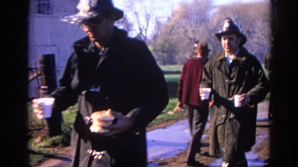 Firefighters in helmets and coats pass close to the camera in Wauconda, Illinois, with smoke and a rural yard behind them.