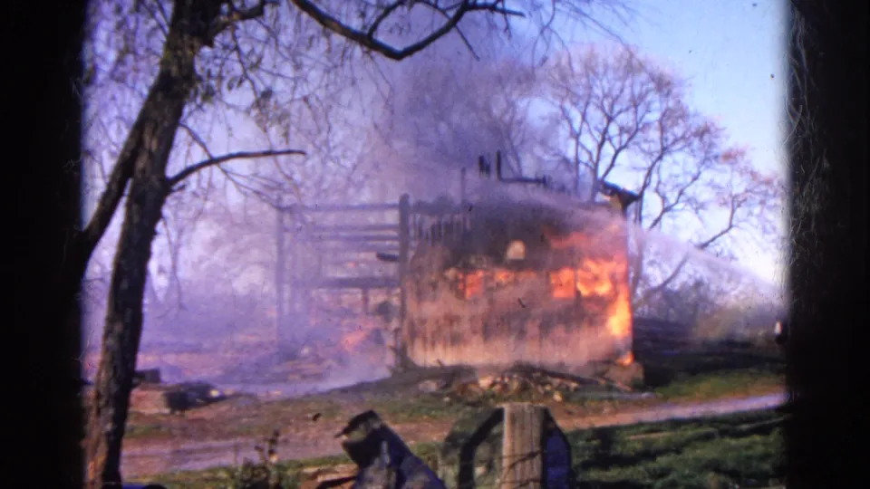 A burning wooden structure sends flames and smoke into the air in this 1968 Wauconda, Illinois home-movie frame.