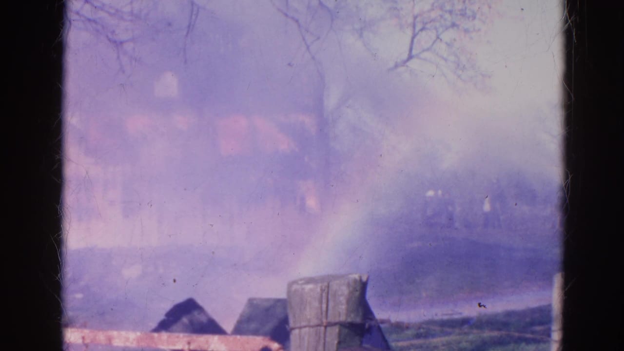 Smoke-filled view of the burning structure with fence posts and dark tree trunks.