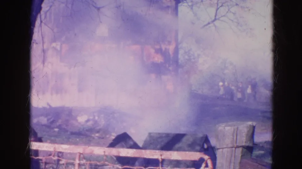 Faded 8mm view from Wauconda, Illinois in 1968, showing smoke, water spray, a wooden fence, and a partially visible burning house.