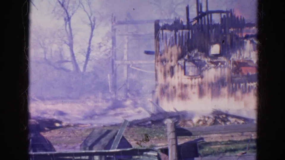 1968 Wauconda, Illinois frame with a blackened wall section, smoky background, bare trees, fallen boards, and debris across the ground.