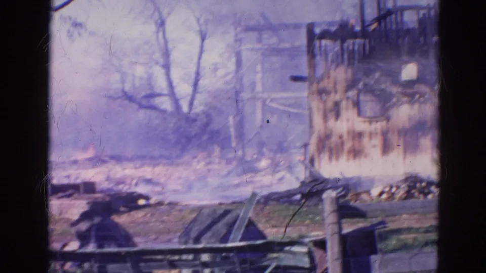 1968 Wauconda, Illinois frame of a burned structure with charred upright wall, smoke or haze, bare trees, fallen boards, debris, and grass.