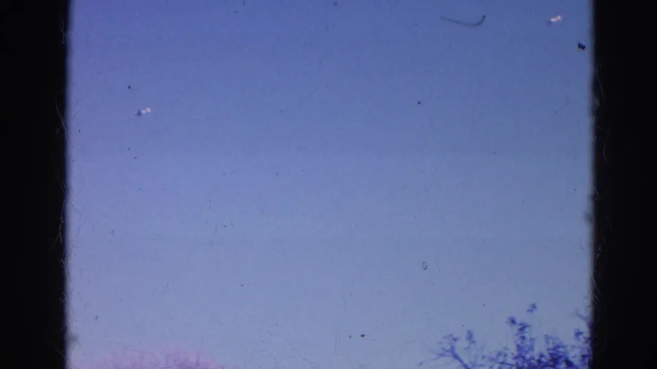1968 Wauconda 8mm frame with blue sky, vertical film gate edges, faint treetops, and small dust marks on the scan.