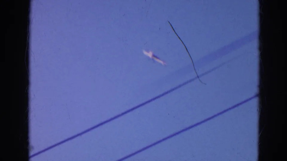 1968 Wauconda 8mm frame showing diagonal utility lines against blue sky and a small bright aircraft-like object near the center right.