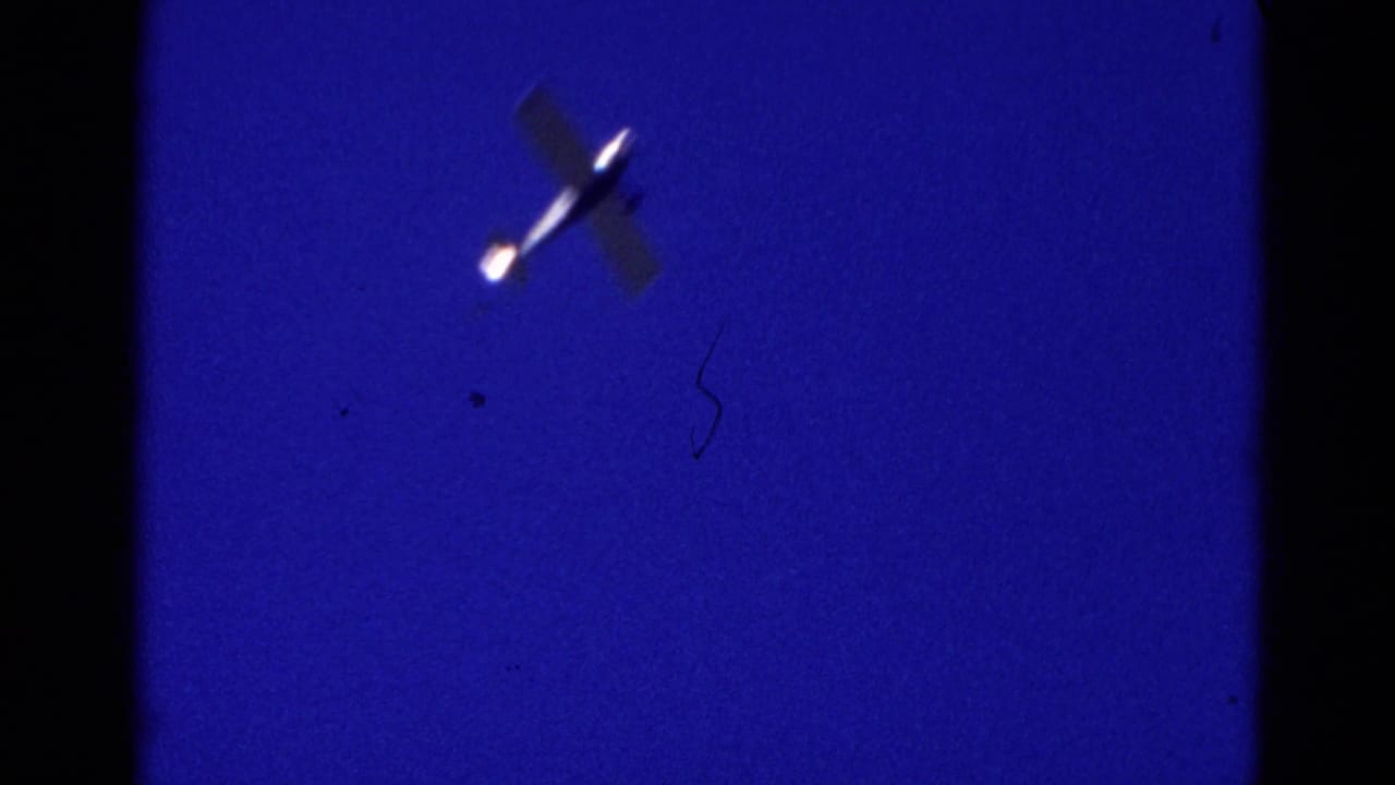 Small plane crossing a deep blue night sky with dark film borders.