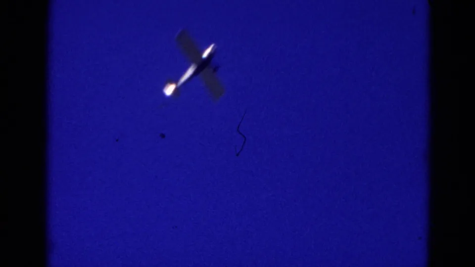 1968 Wauconda 8mm frame showing a small plane lit against a saturated blue night sky, with film edge shadows visible.