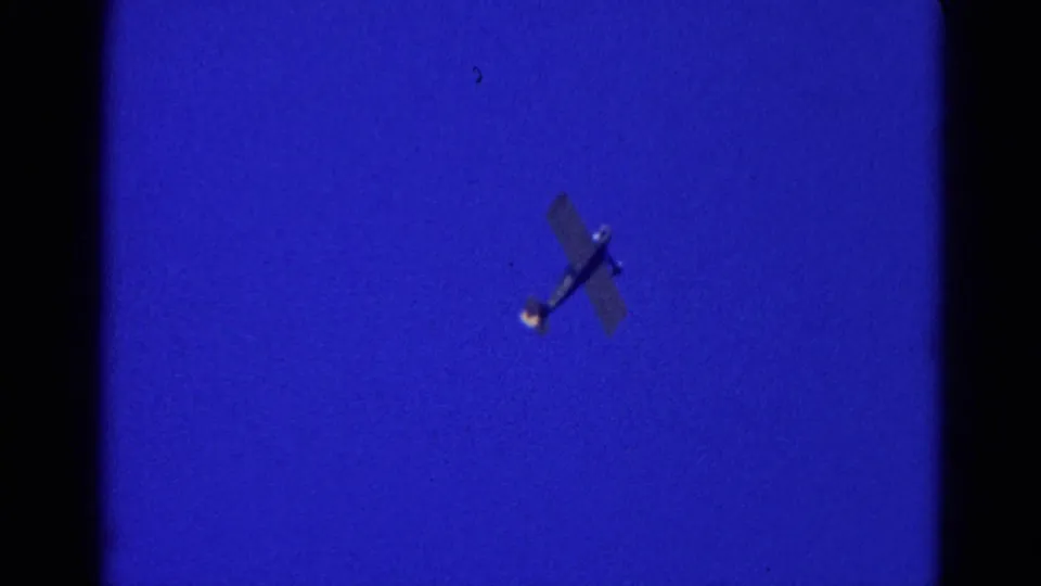 Small aircraft appears angled over Wauconda, Illinois at night in this 1968 8mm frame, with saturated blue exposure and soft grain.