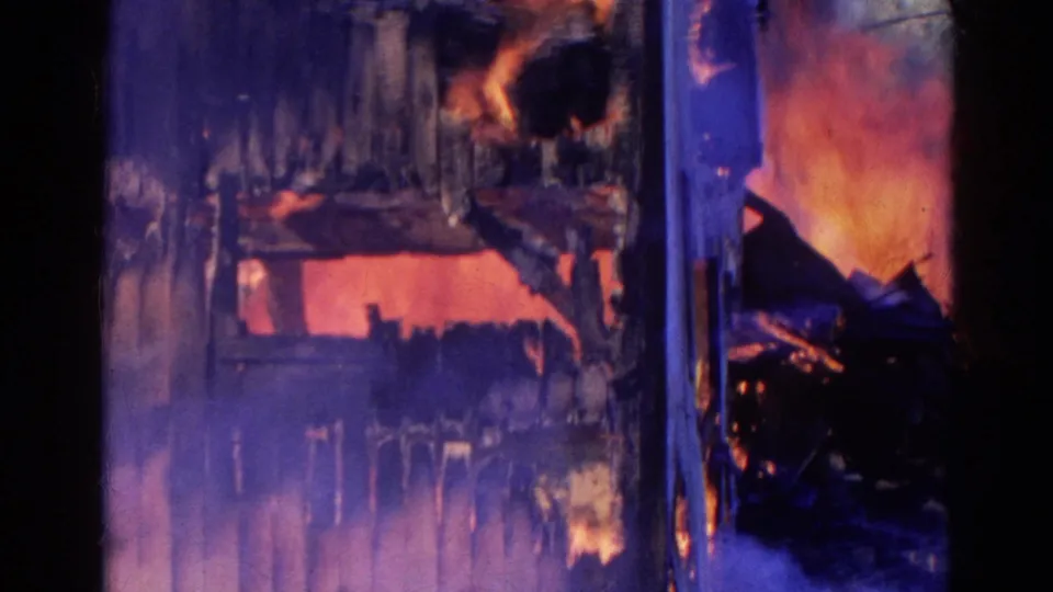 1968 Wauconda 8mm frame showing a structure engulfed in orange flames and smoke, with dark debris and blue-toned night exposure.