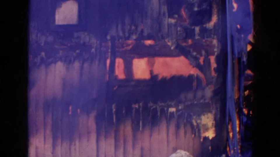 1968 Wauconda 8mm frame showing flames inside a damaged wooden wall, with smoke staining across the structure.