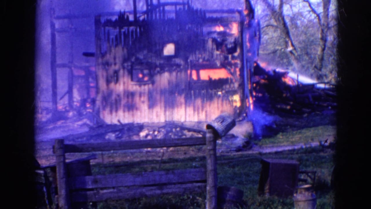 Burning structure with smoke and a hose stream reaching in from the right side.