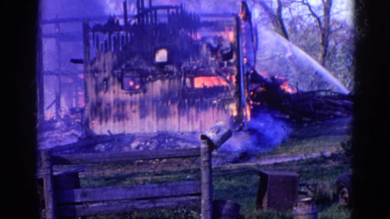 1968 Wauconda 8mm frame with water spraying across a yard toward a burning wooden structure behind a fence.