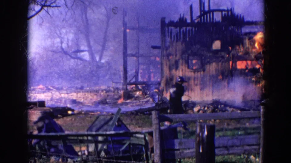 A firefighter stands near the smoking remains of the burning barn in Wauconda, Illinois, with flames still visible inside the frame.