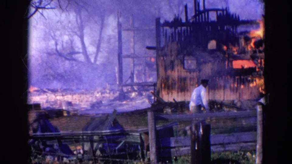 The Wauconda fire scene shows the man continuing past the fence while smoke and flames remain visible in the damaged house.