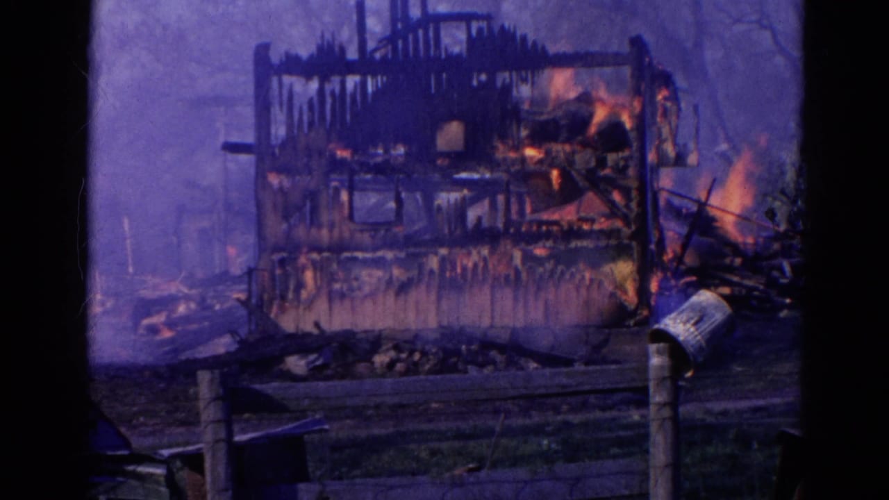 1968 Wauconda, Illinois 8mm frame showing a fire-damaged wooden structure burning behind a low fence and dark foreground frame.