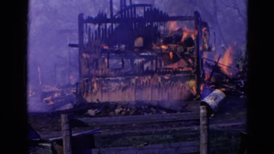 1968 Wauconda, Illinois 8mm frame showing a fire-damaged wooden structure burning behind a low fence and dark foreground frame.