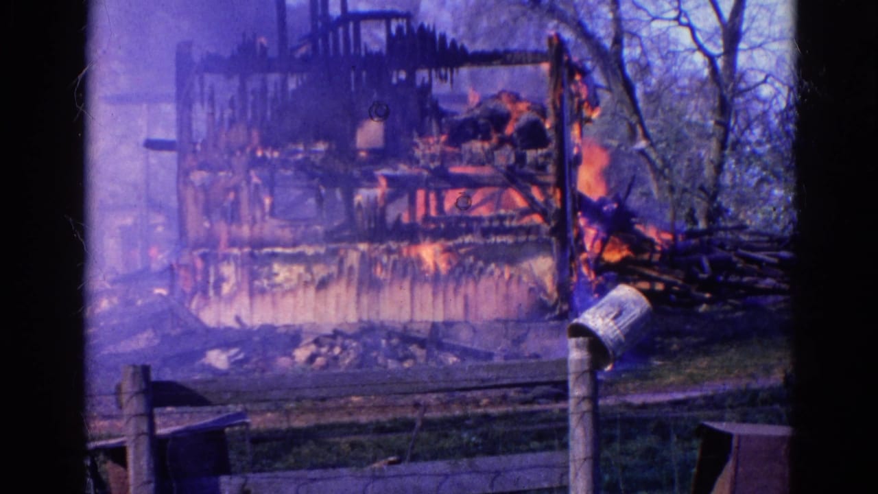 Vintage 8mm frame from Wauconda, Illinois showing a charred structure with active flames, smoke, fence posts, and trees nearby.