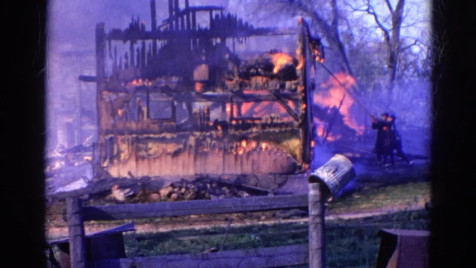 1968 Wauconda, Illinois frame showing a firefighter near a burning wooden structure as smoke and flames fill the background.