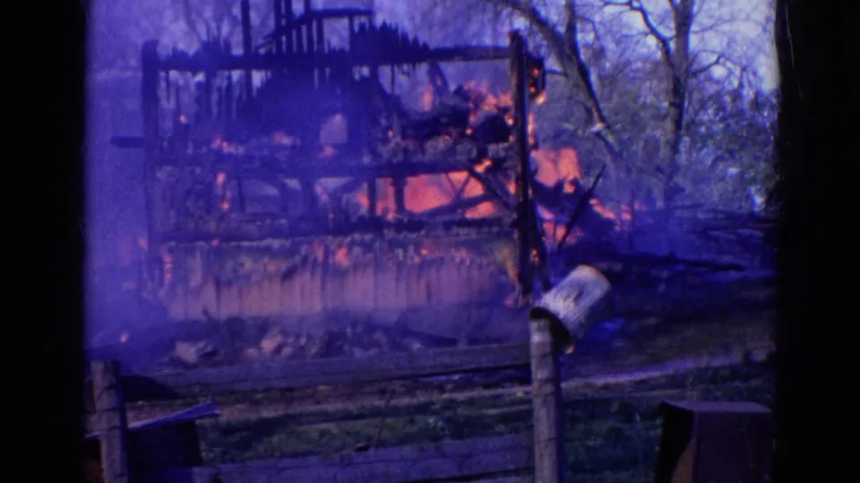 1968 Wauconda 8mm frame with heavy blue smoke over a burning wooden structure and a person working near the right edge.