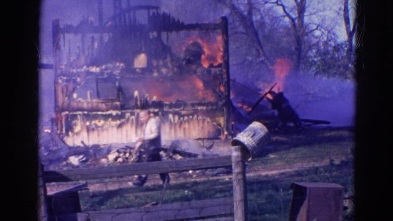 Burning wood structure with smoke, yard fence, and a person near the flames.