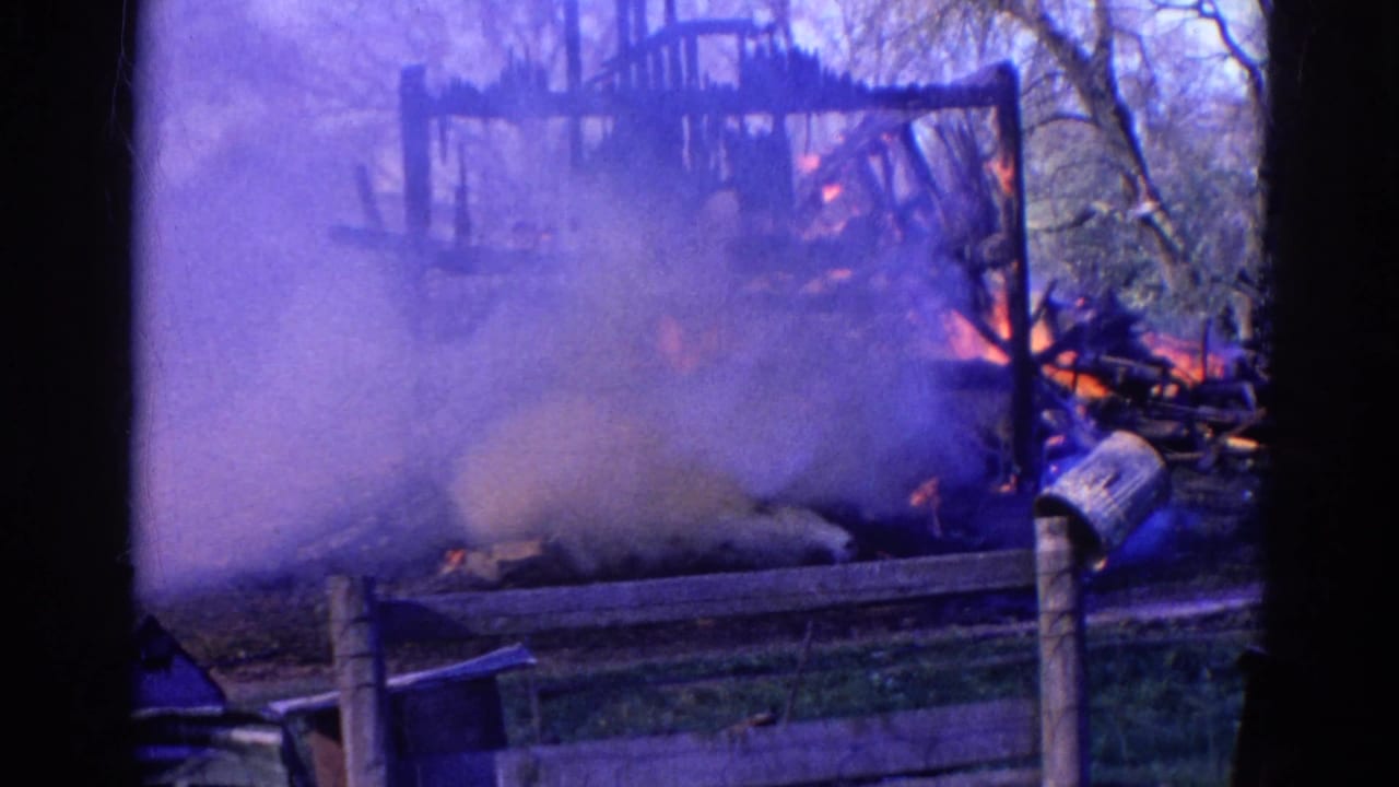 Smoke and flames surround a burning wooden structure behind a fence.