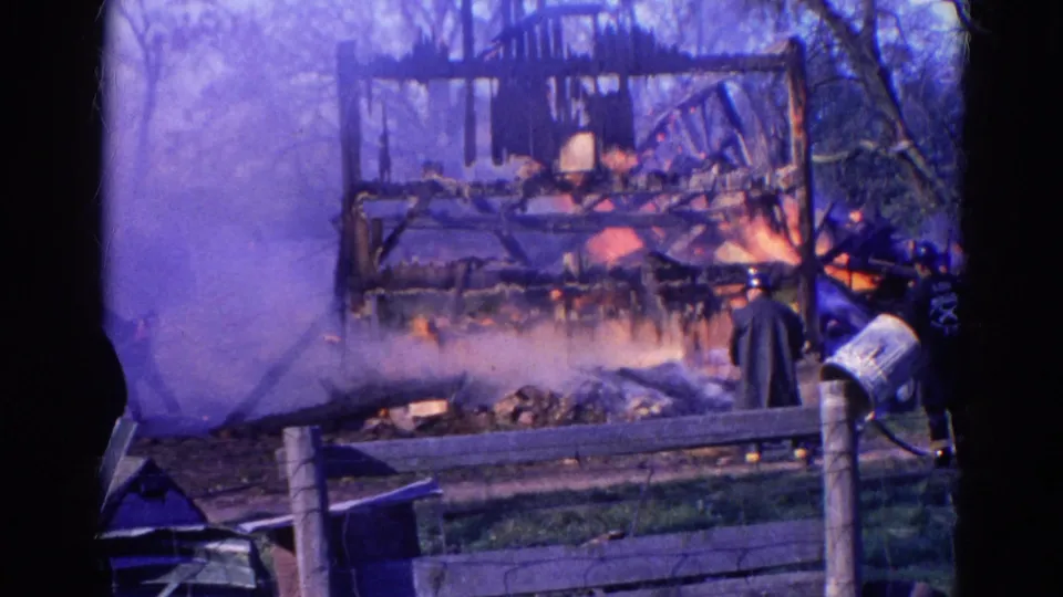 1968 Wauconda, Illinois fire scene with visible figures near smoke, flames, a fence, and a charred wooden frame.