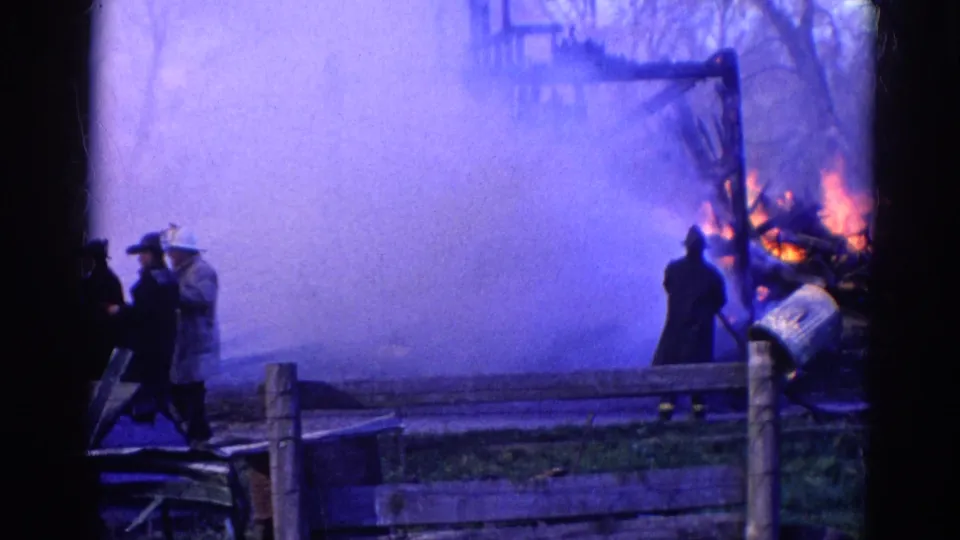 1968 Wauconda, Illinois 8mm frame with figures near a fence as smoke obscures part of a burning structure.